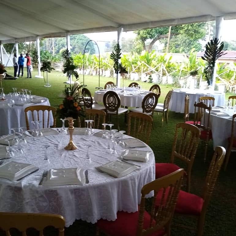 Tables rondes dressées et chaises dorées sous une tente de réception