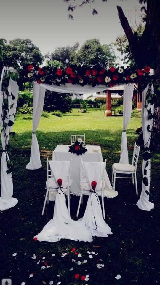 Arche de cérémonie drapée de blanc et fleurs rouges dans le jardin du Clos des Roses