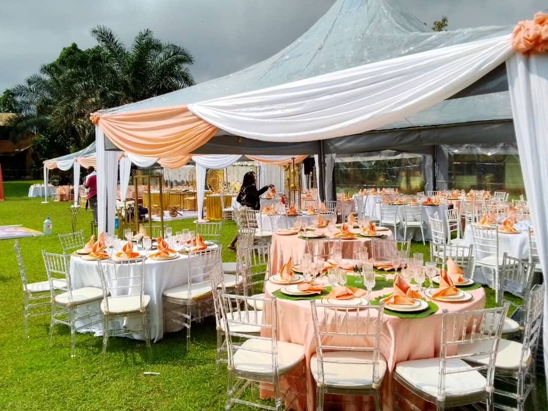 Réception sous tentes avec nappes pêche et chaises transparentes sur la pelouse